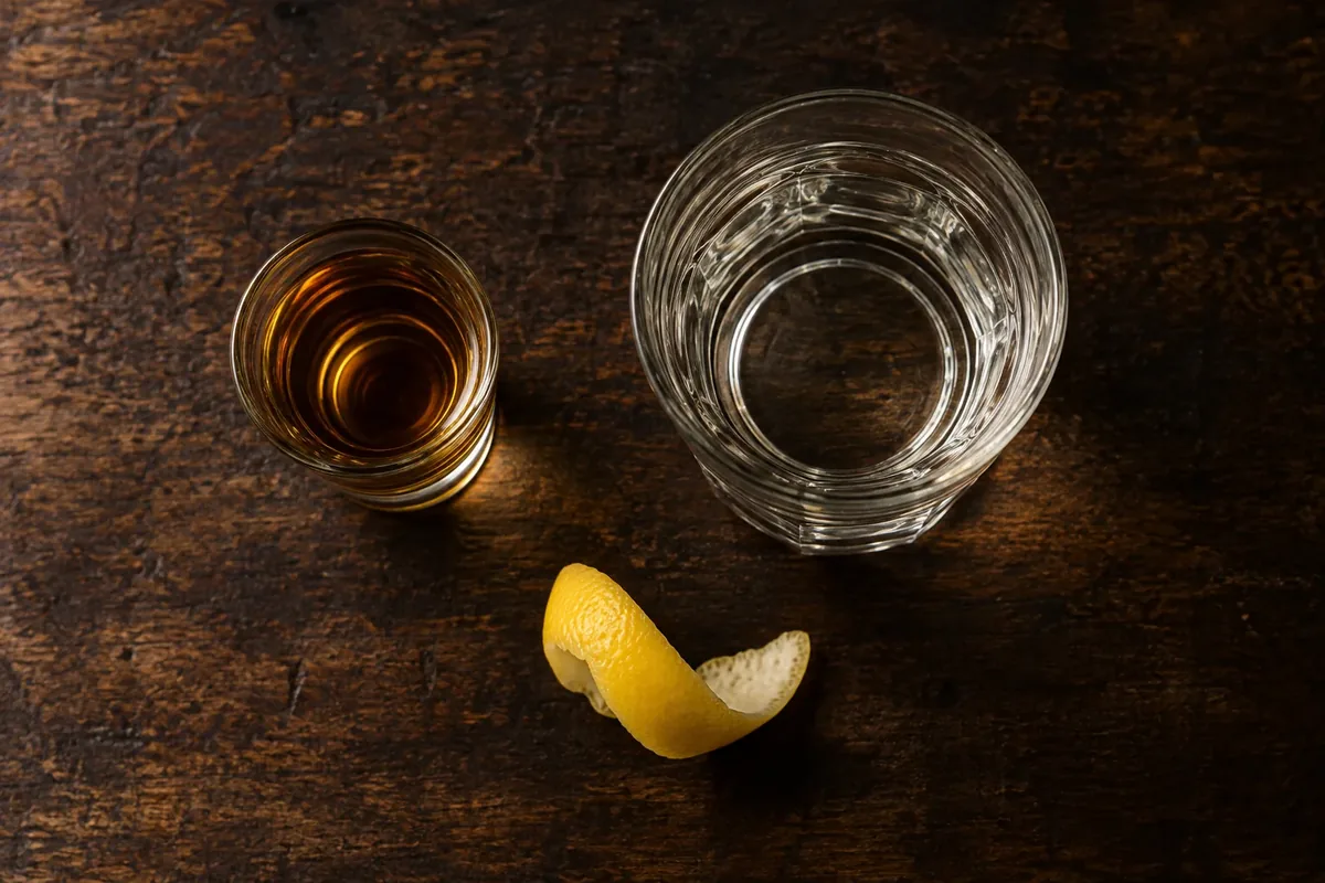 A small measured almond-liqueur sample beside a larger clear base-spirit measure and lemon peel