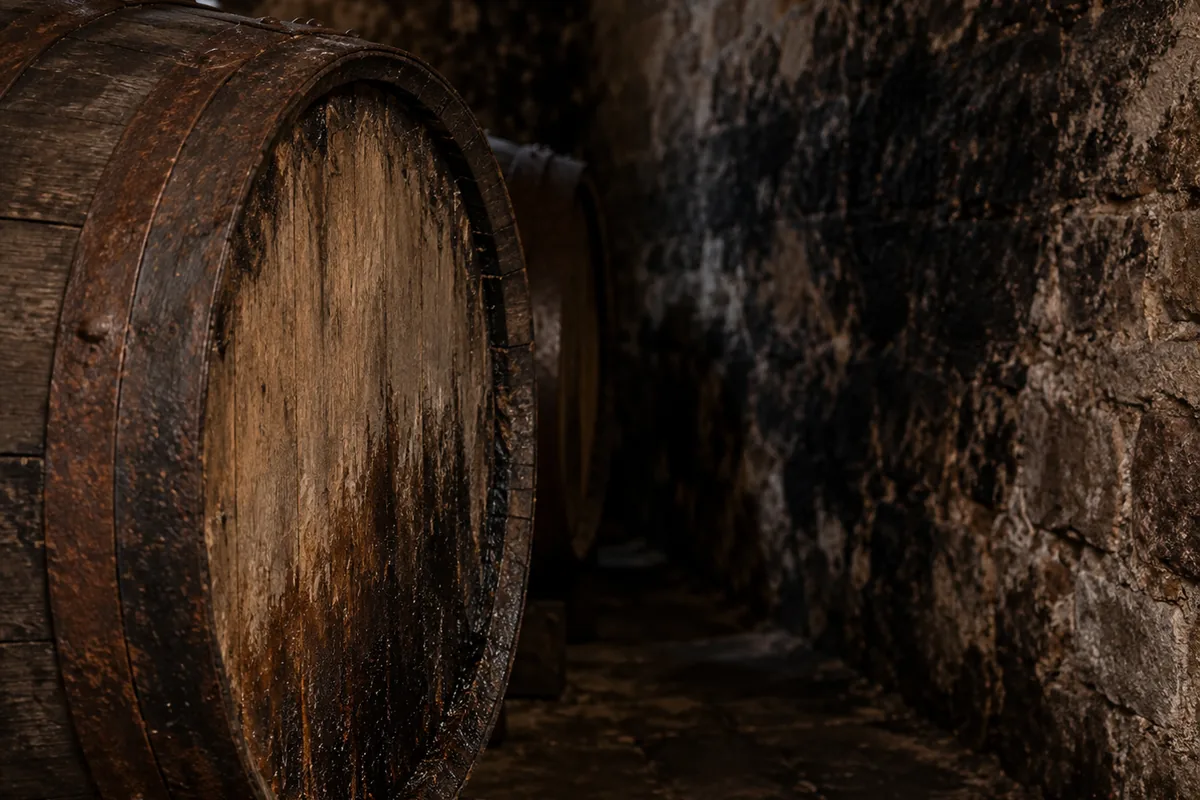 The damp end of a cask in a warehouse with a dark sooty bloom spreading across the stone wall behind it