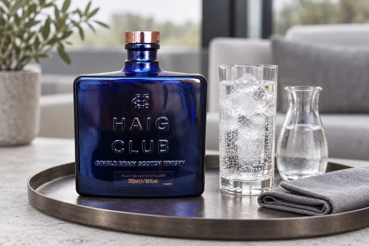 A recognizable blue Haig Club Single Grain Scotch bottle served with a tall highball and water carafe on a modern lounge tray.