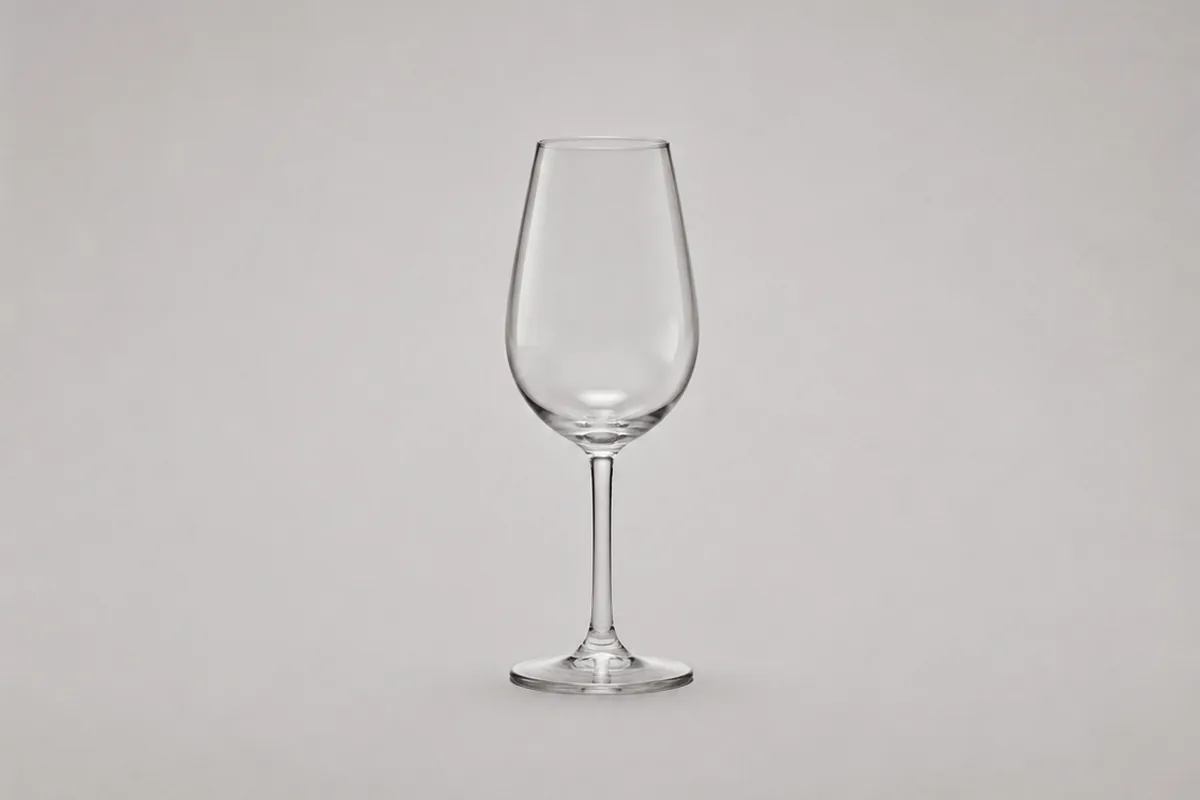 An empty clear stemmed glass standing alone on a plain pale grey background, its bowl an elongated egg that swells at the middle and draws in to a narrower opening at the rim, the whole glass from rim to foot inside the frame.